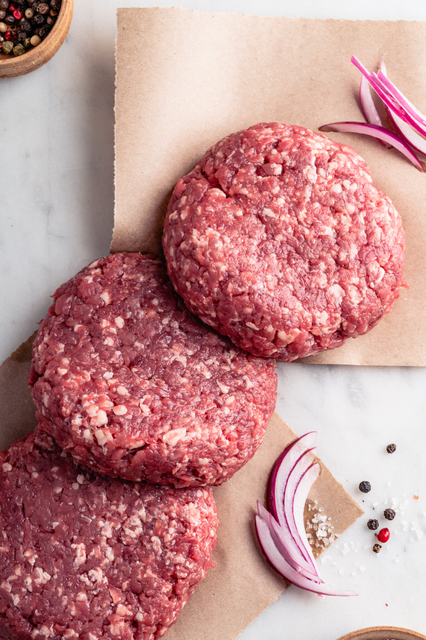 Raw homemade burger steak cutlets and spices on craft paper, high angle view