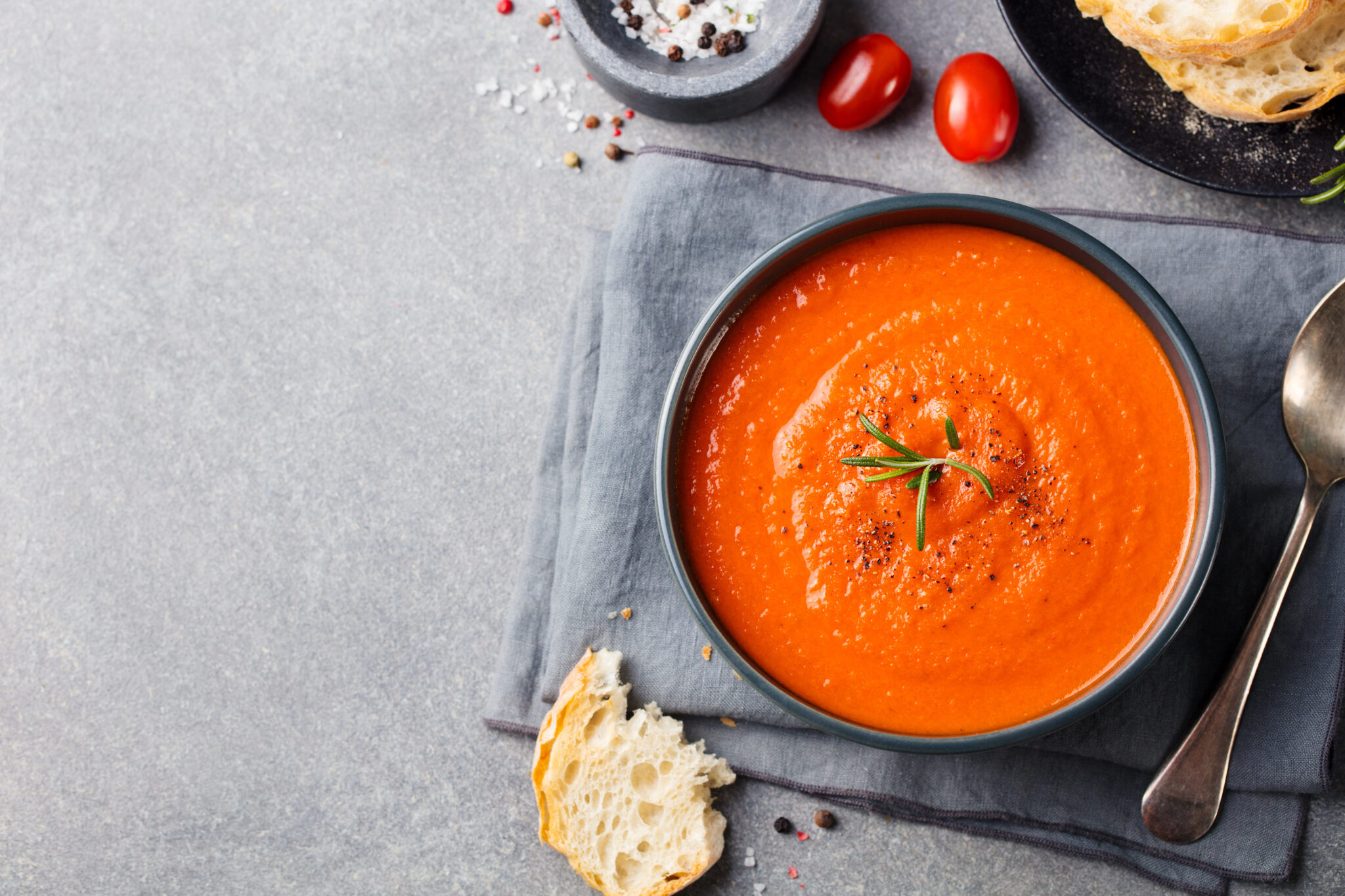 Tomato soup in a black bowl on grey stone background. Top view. Copy space